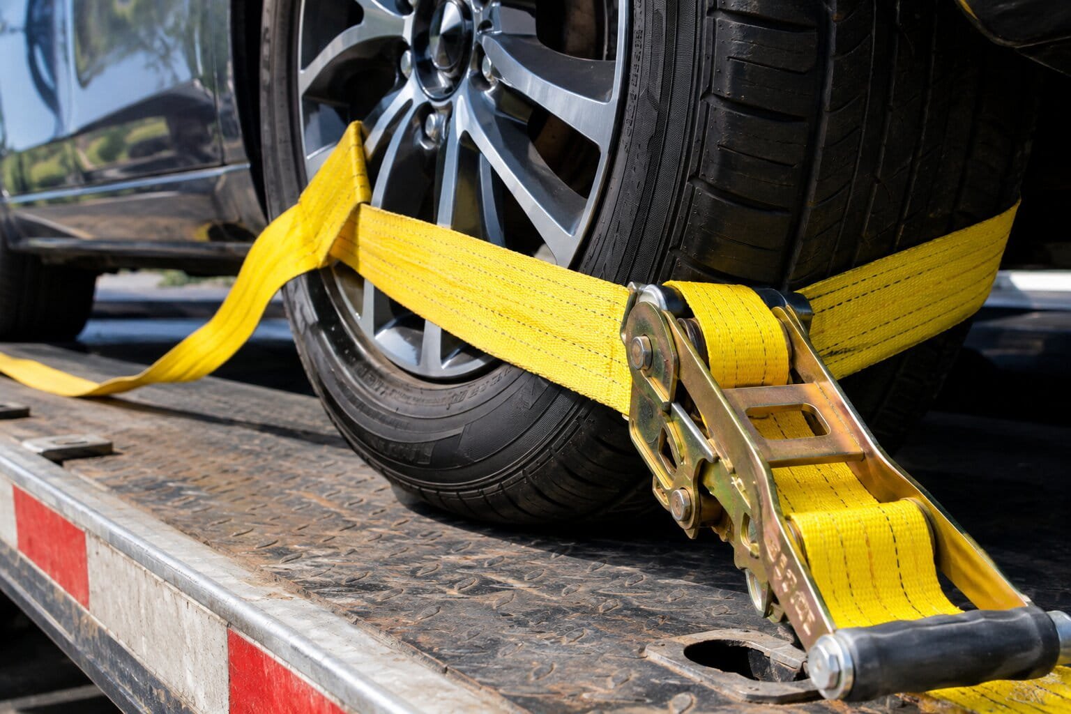 Wheel net strap securing a tire to a flatbed tow truck deck